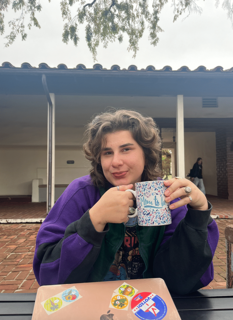 Willow sitting with a mug in their hand in a courtyard