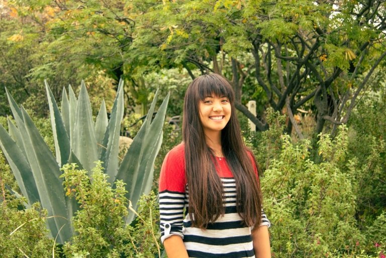 Shelby Ottengheime wears a red, blck, and white striped sweater while standing in front of succulents.