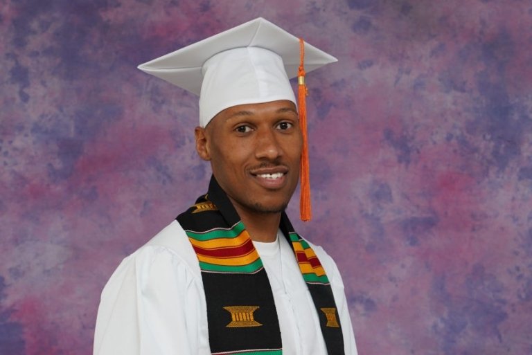 Close-up of Yusef Pierce wearing the white Pitzer graduation regalia and Kente cloth stole.
