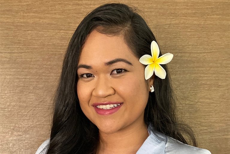 Close-up of Corina Penaia wearing a plumeria in her long dark hair.