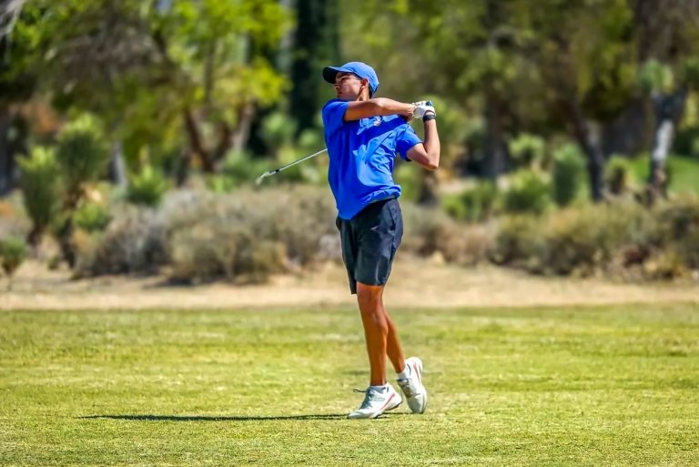A member of the Pomona-Pitzer men's golf team swings a club on a green field.