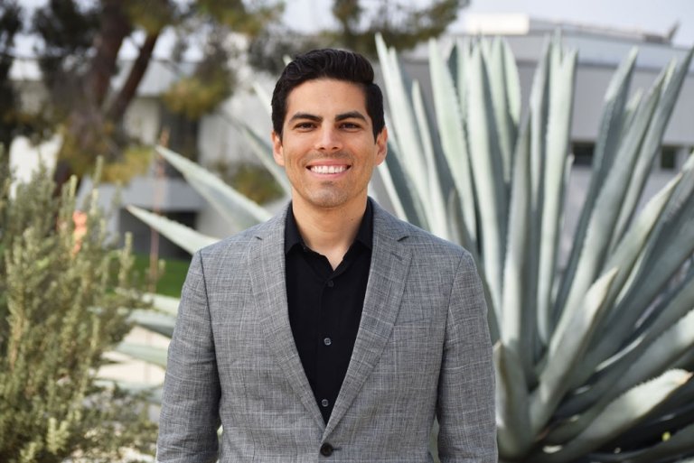 Marcus Rodriguez has short black hair and wears a gray blazer over a black shirt.