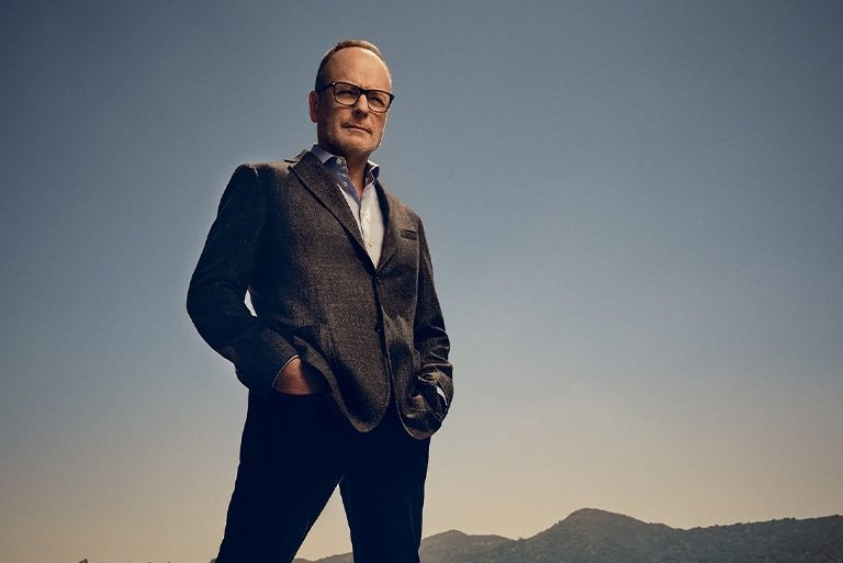 John Landgraf wears black-rimmed glasses and a dark suit jacket over a white collared shirt.