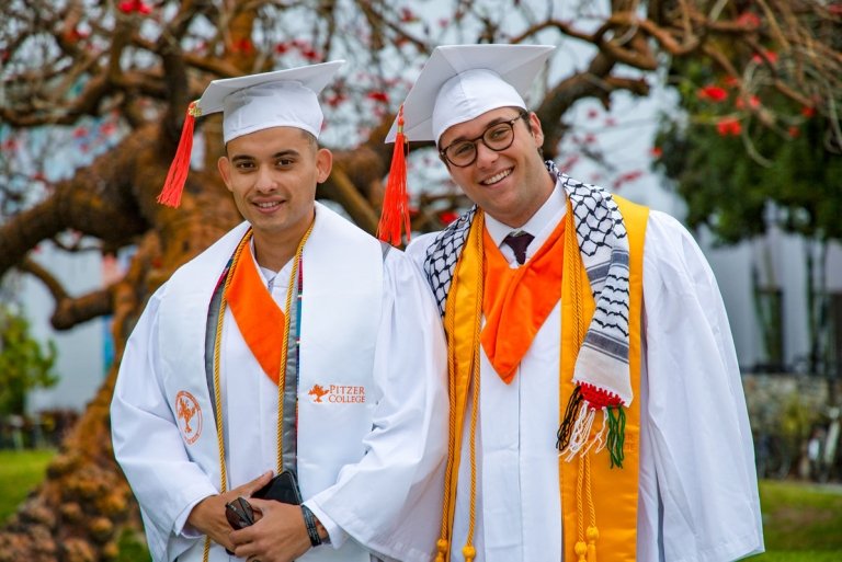 Ryan C. and Stryder Rodenberg wear their white graduation regalia and caps with orange tassels and different colored stoles and cords.