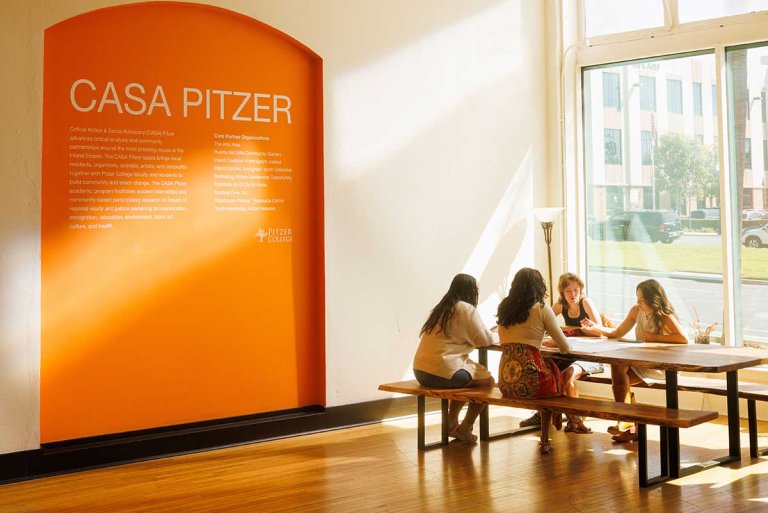 students sit at a table next to the large orange casa pitzer sign