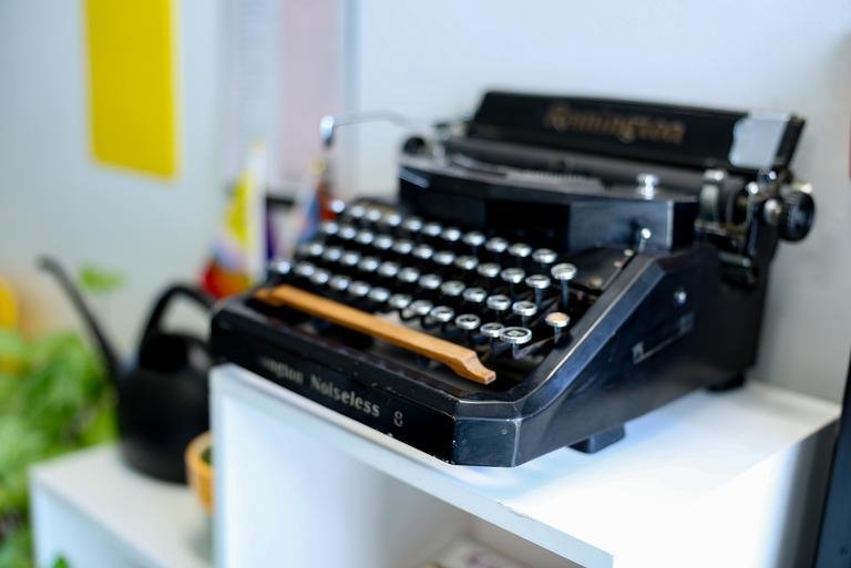 a black typewriter sitting on a white bookcase in the writing center