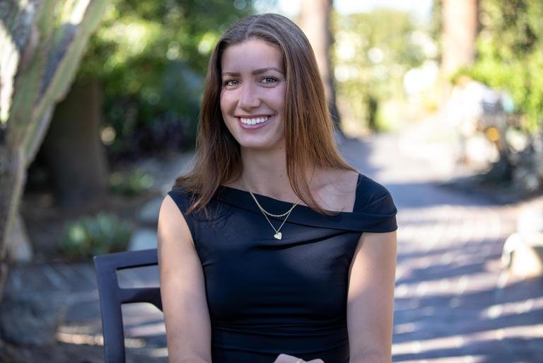 a young woman with brown hair and a black top smiles at the camera