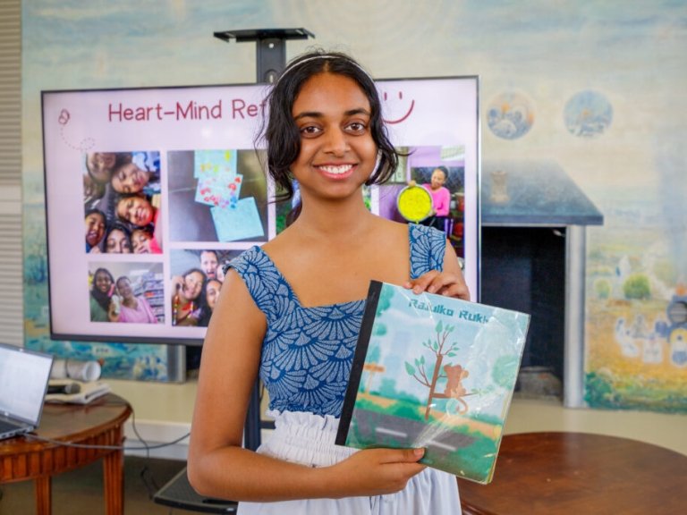 Pratya Poosala holds up a children's book she created in Nepali with an illustration of a monkey on a tree.