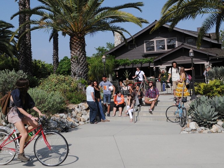 an exterior shot of the grove house with several students hanging out on the steps in front
