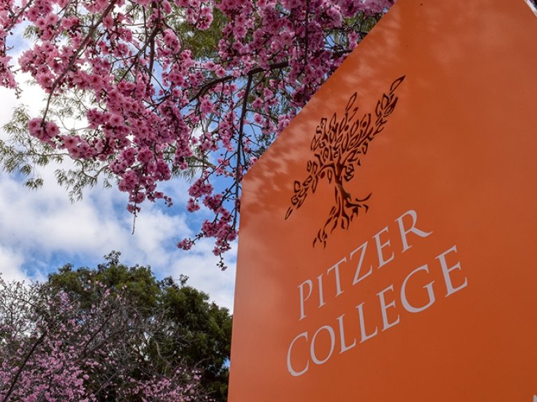 An outdoor Pitzer College orange sign surrounded by cherry blossoms