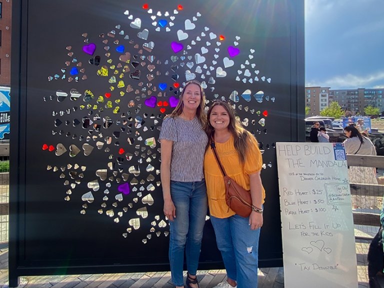 Elizabeth Faraci stands to the right of another person in front of The Mandala Project artwork.