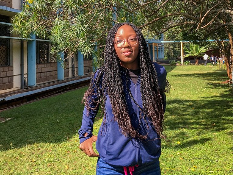 Sia Were wears a navy blue jacket and glasses and has long black hair in braids.