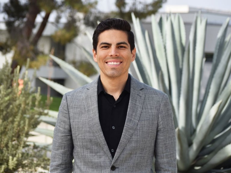 Marcus Rodriguez has short black hair and wears a gray blazer over a black shirt.