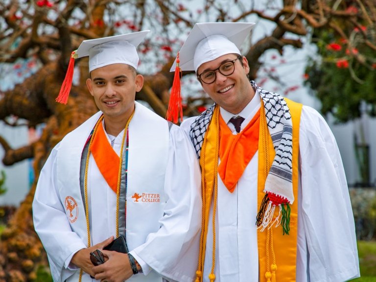 Ryan C. and Stryder Rodenberg wear their white graduation regalia and caps with orange tassels and different colored stoles and cords.