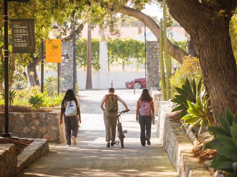 three students walk down pitzer walk toward pitzer gate