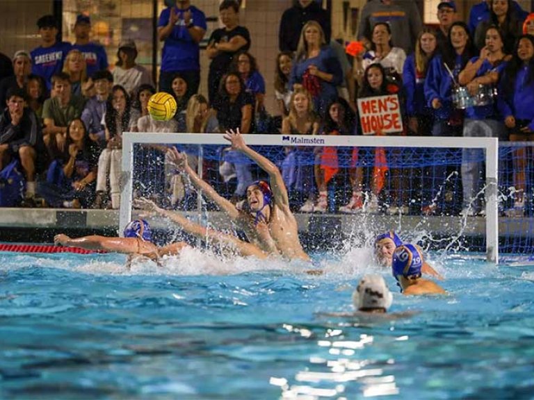 action shot of a mens water polo game with spectators in bleachers in the background