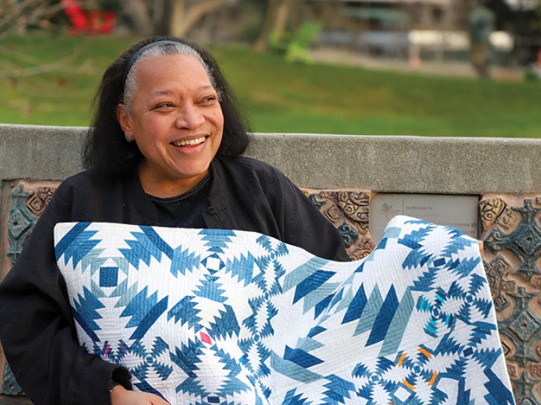 Chawne Kimber sits on a bench on the mounds while holding one of her quilts