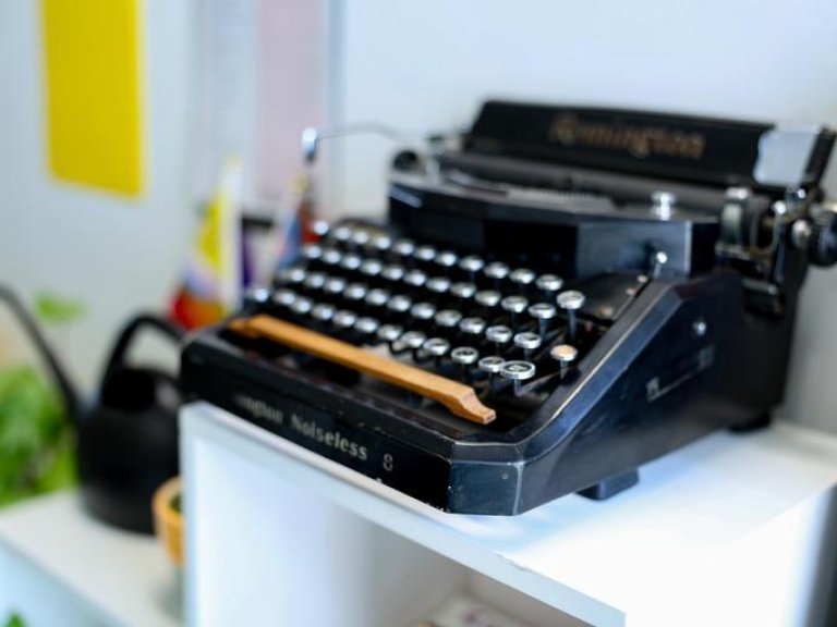 a black typewriter sitting on a white bookcase in the writing center