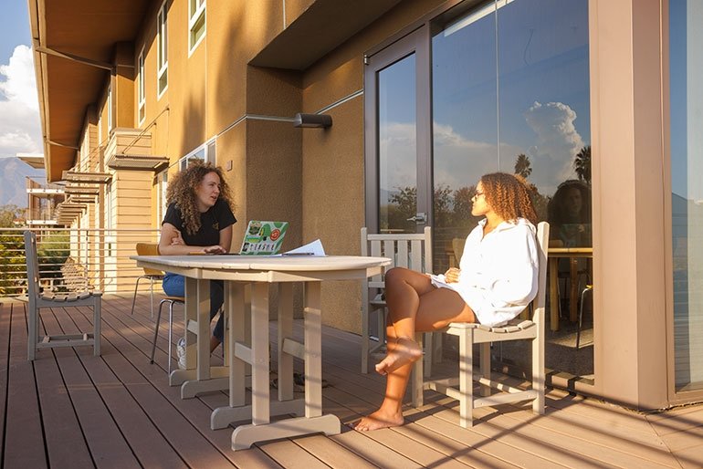 Two students sit at tables outside a dorm room