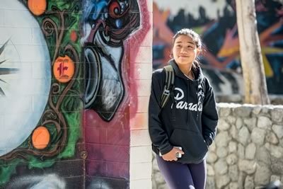 A student in a black hoodie leans against a wall with a mural.