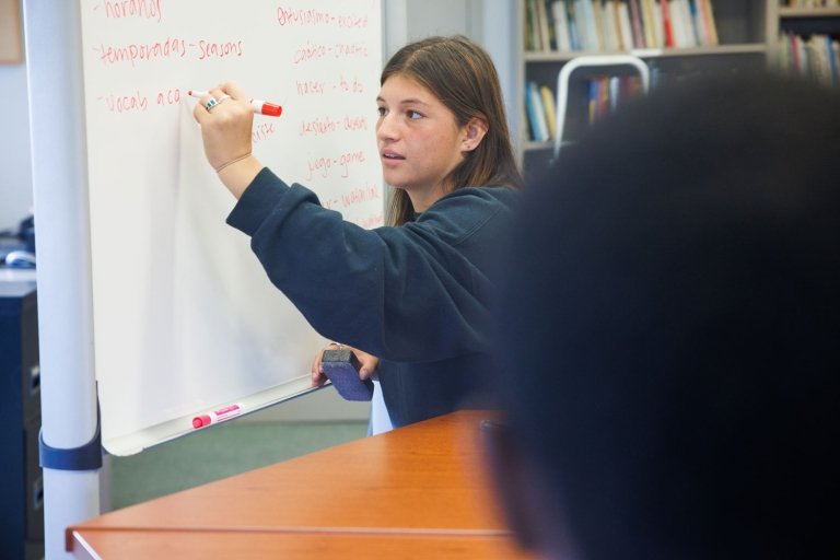 A student writes Spanish words on a whiteboard.