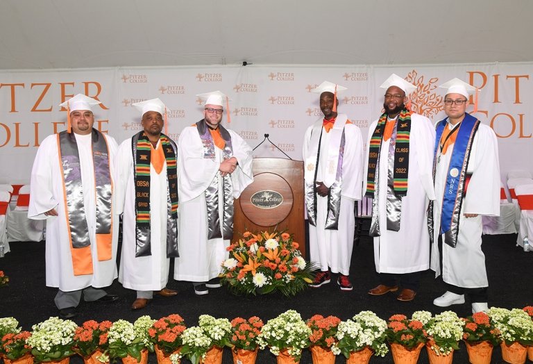 Pitzer's first inside-out graduating cohort pose on a stage in graduation gowns