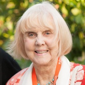 Close-up of Margreta Klassen, who has straight white hair cut in a bob and wears an orange and white top.