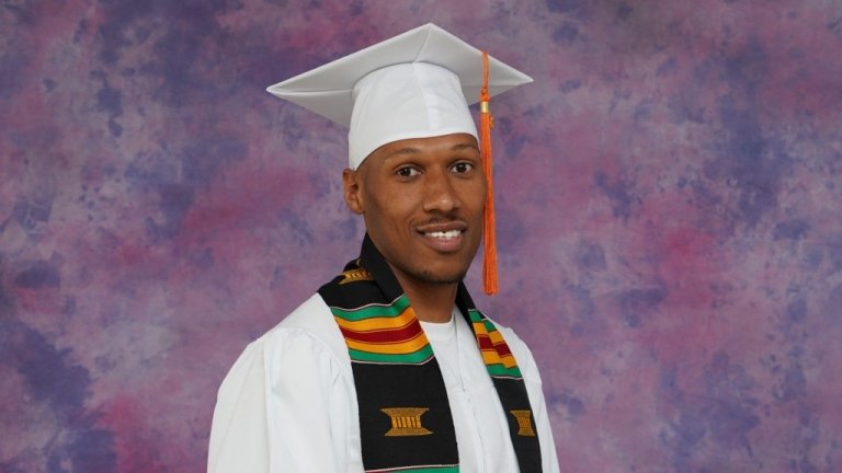 Close-up of Yusef Pierce wearing the white Pitzer graduation regalia and Kente cloth stole.