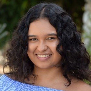 Headshot of Adriana M. Ceron, who has wavy dark hair and wears a light blue top.