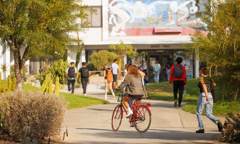 several students walk across the mounds with mead hall entrance in the background