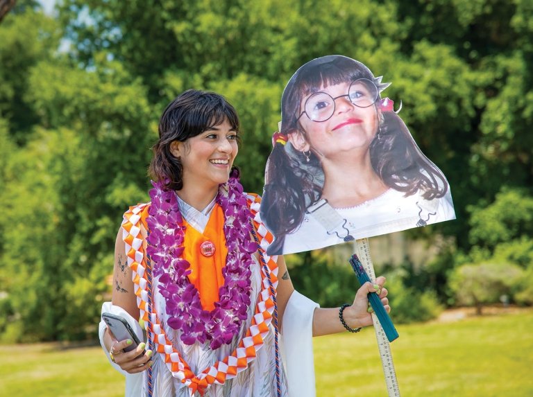 commencement student holding gifts for a posed photo in front of grass