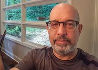 Dan Segal with brown shirt sitting in front of window