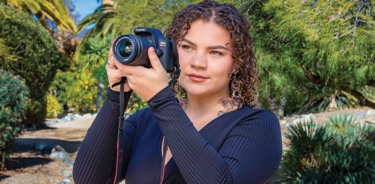 Jansikwe Medina-Tayac poses with a camera in front of the Grove House