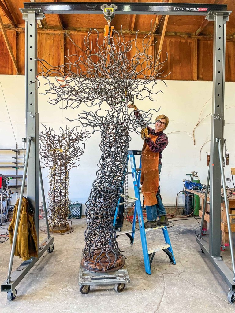 Pitzer alumna Marguerite Elliot stands next to a large sculpture made of rebar