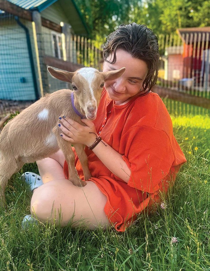 Wynne chase sits on the grass with a baby goat on her lap