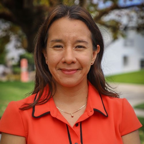 Closeup of Alma Bezares Calderon, who has straight brown hair and wears an orange collared top.