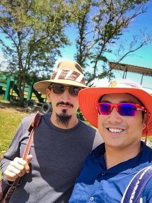 A selfie of James Kang (right) and James Brunswick (left) at the Dominican Republic. Kang wears an orange hat and sunglasses and blue shirt. Brunswick wears a tan hat, sunglasses, and a gray shirt.