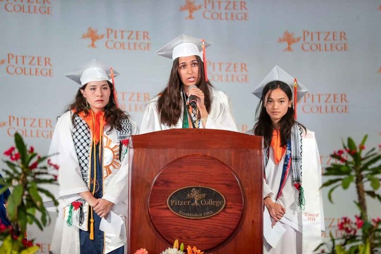 three students wearing kaffiyehs stand onstage at the podium during Pitzer's 2024 commencement