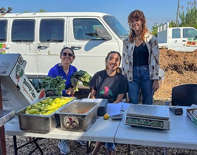 Andrea Robinowitz stands behind a produce table with two other people at Huerta de Valle