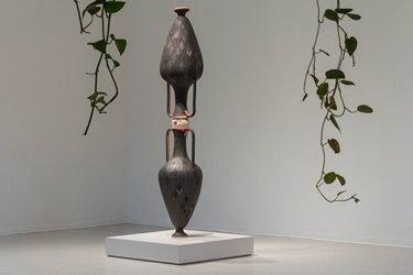 Two vases stacked on top of each other with two strands of pathos plants hanging on each side