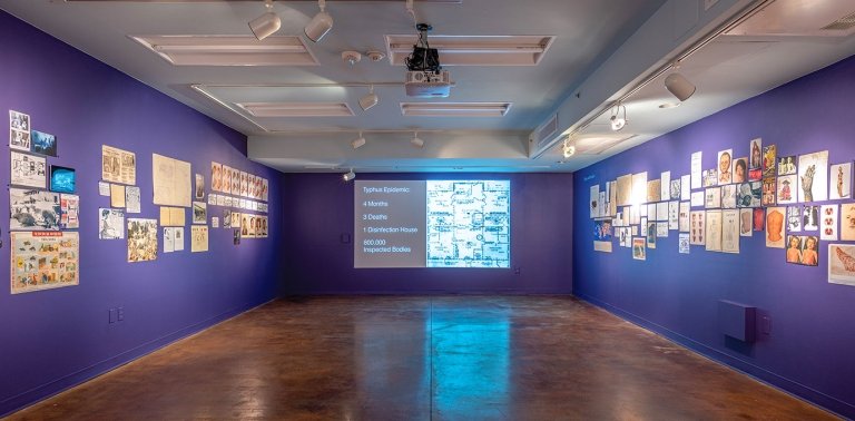 view of an art gallery with blue walls, items hung on the wall, and a screen with an image projected on it