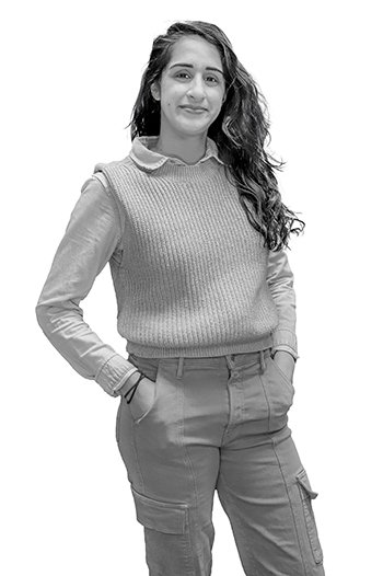 portrait of a woman with long dark hair wearing a sweater vest, pants, and a collared shirt