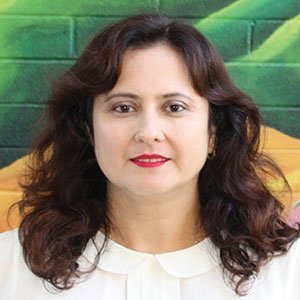 a woman with shoulder-legnth brown hair wears a white blouse with a peter pan collar as she stands in front of a colorful wall
