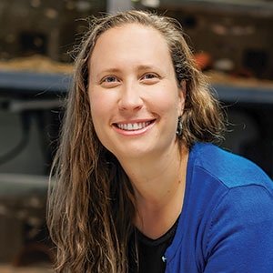 portrait of a woman with long light brown hair wearing a blue cardigan and black shirt
