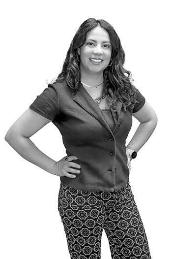 a black and white portrait of a woman with long brown hair wearing patterned pants and a dark button up shirt
