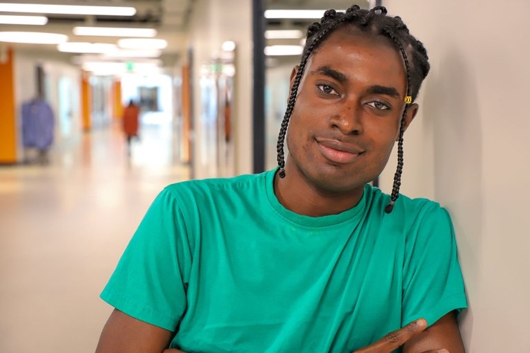 richard ampah leans against a wall in a wallway of nucleus west