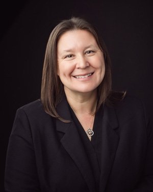 Diana Bob has long straight brown hair and wears a black blazer.