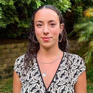 Close-up of Ariella-Seidman-Parra wearing a black and white patterned shirt and with long wavy dark hair.