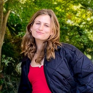 Close-up of Charlotte Wirth with long wavy blond hair and wearing a dark blue jacket over a red shirt.