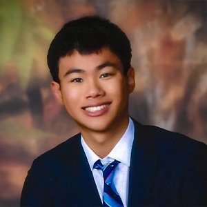 Close-up of Grant Ho with short black hair and wearing a black suit jacket over a white collared shirt and a striped tie.